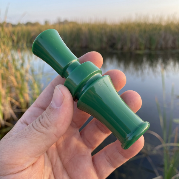 Hand holding the green waterfowl duck call whistle, showing its size